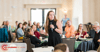 Woman presenting in a conference room full of people.