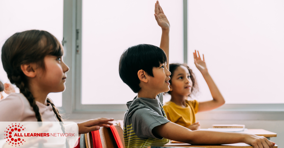 Three children sitting at desks. Two raising their hands