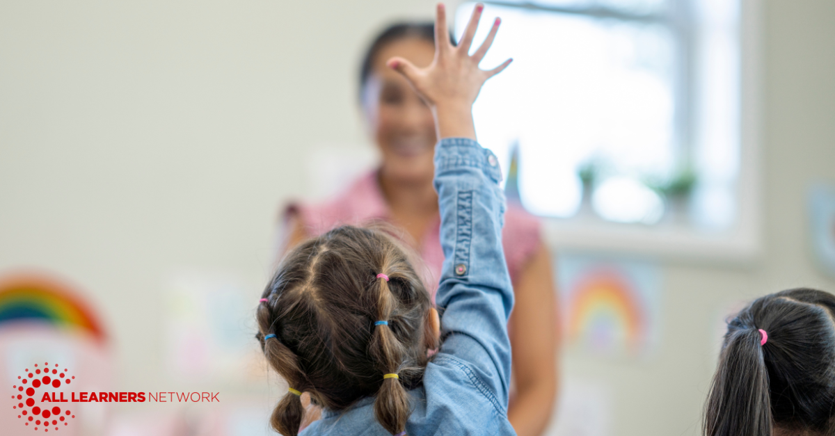 Student raising hand with female teacher looking on